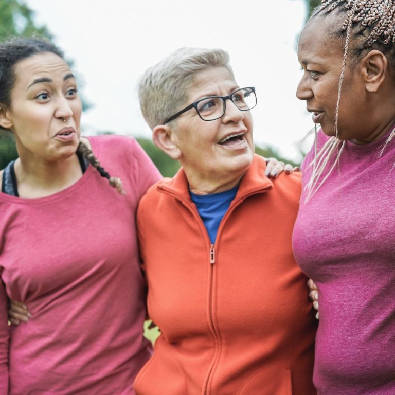 Three women smile and interact outdoors, showing joy and camaraderie.
